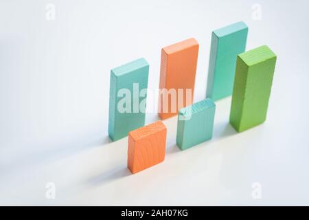 Two parallel rows of blue, orange and green flat wooden bricks making up financial charts over white background Stock Photo