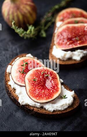 Tasty rye bread toast with cream cheese and fresh ripe figs. Healthy appetizer or snack. Black concrete background Stock Photo
