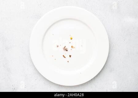 White plate with crumbs leftovers on grey concrete background. Top view Stock Photo