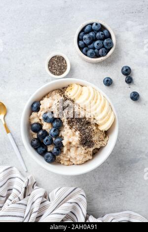 Oatmeal porridge in bowl with blueberries, banana and chia seeds on a grey concrete background, healthy breakfast food. Top view. Vertical composition Stock Photo
