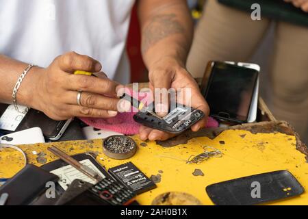 A Filipino man repairing a mobile phone on a side street within Cebu City,Philippines Stock Photo