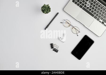 Wireless earphones, eyeglasses, pen, clips, smartphone, small plant and laptop Stock Photo