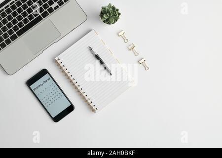 Notebook with pen, monthly planner in gadget, clips and other stuff on desk Stock Photo