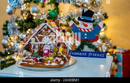 Selective focus on home decorated ginger bread house on a white table in front of a decorated Christmas tree Stock Photo