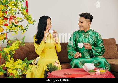 Happy young couple celebrating Chinese New Year and drinking tasty tea with sweet dried fruits and berries Stock Photo