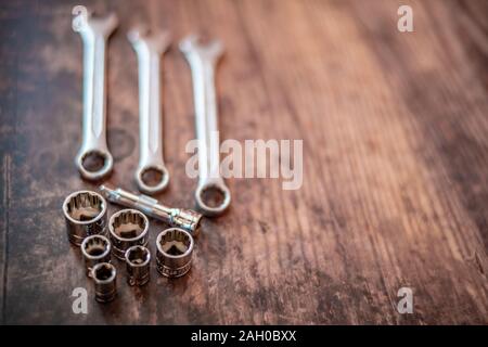 Selective focus of wrench sockets with out of focus spanners on a plain wooden background Stock Photo