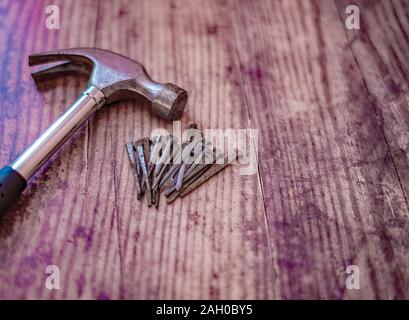 Claw hammer and pile of rusty nails on a plain wooden background Stock Photo