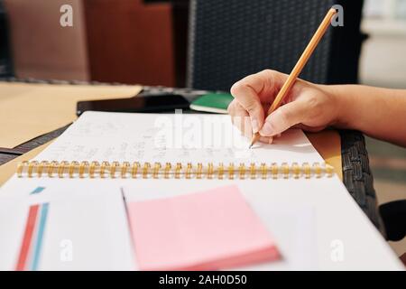 Close-up image of student sitting at cafe table and writing in textbook Stock Photo