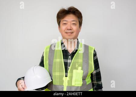 Asian middle-aged man in a Light green work vest and white safety hat. Stock Photo
