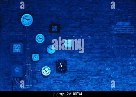 Collection of vintage wall clocks hanging on an old brick wall in blue colors. Color of the 2020 year. Stock Photo