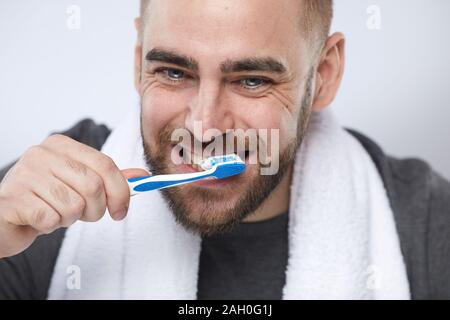 Horizontal close up portrait shot of yong man with beard on face brushing his teeth in the morning Stock Photo
