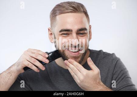 Head and shoulders studio portrait shot of handsome young man smiling while grooming his beard, white background Stock Photo