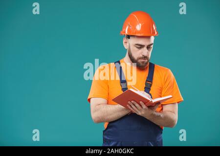 Waist up studio portrait shot of young male laborer wearing uniform writing something in notebook Stock Photo