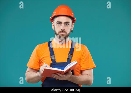 Studio medium portrait shot of Caucasian engineer in workwear making notes looking at camera Stock Photo