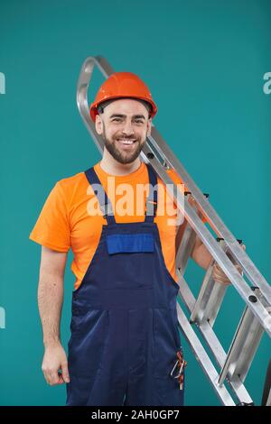 Studio portrait of young adult male electrician holding portable ladder looking at camera smiling Stock Photo