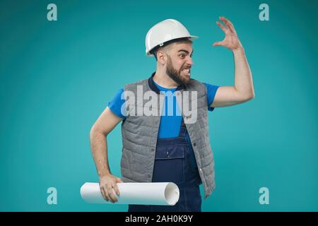 Studio medium portrait shot of construction foreman getting angry with someone about something, blue turquoise background Stock Photo