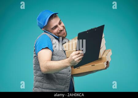 Horizontal medium studio shot of delivery man holding pizza boxes, talking on phone and checking order list Stock Photo