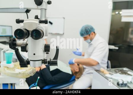 Doctor used microscope. Dentist is treating patient in modern dental office. Operation is carried out using cofferdam. Client is inserted and restored Stock Photo