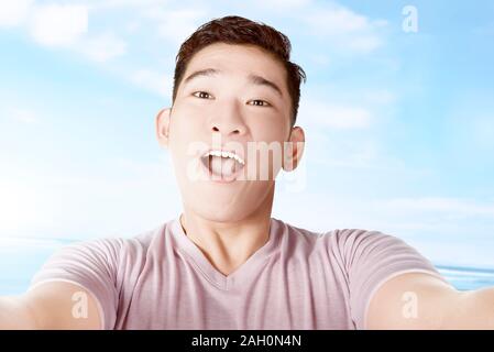 Asian man making selfie using the camera phone with a blue sky background Stock Photo