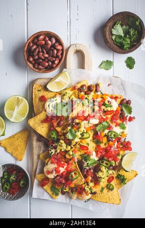 Nachos chips with cheese sauce, guacomole, salsa and vegetables on the board. Party food concept. Mexican food concept. Stock Photo