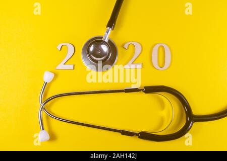 2020 in wooden figures and black stethoscope on yellow background Stock Photo