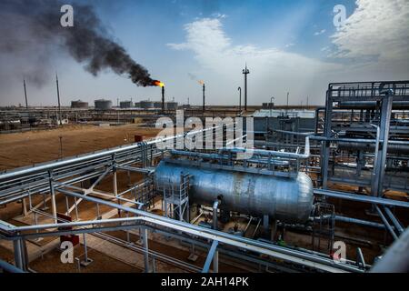 Grey pipes and orange burning gas torch of an oil refinery plant in the yellow desert. Blue sky with clouds. Panorama view Stock Photo