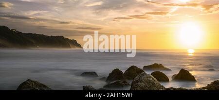 Stunning view of a rocky coast bathed by a smooth silky sea during sunset. Melasti Beach with its cliff in the distance, South Bali, Indonesia. Stock Photo