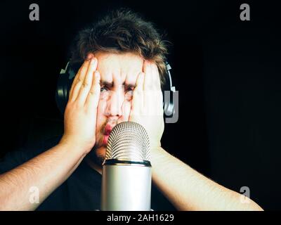 Young bearded man plays video games with mic for voice and headphones. Guy leads online stream and sad because fail in game Stock Photo