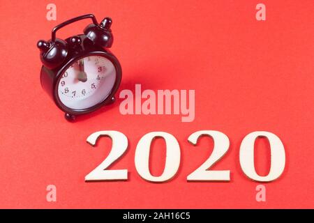2020 in wooden figures and black alarm clock on red background Stock Photo