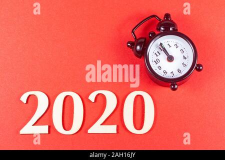 2020 in wooden figures and black alarm clock on red background Stock Photo