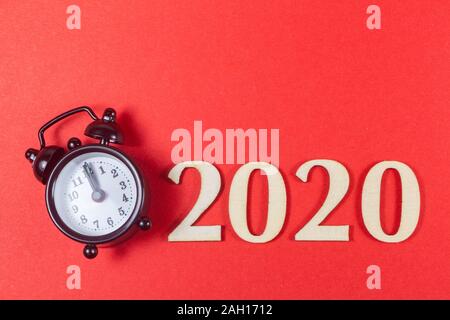 2020 in wooden figures and black alarm clock on red background Stock Photo