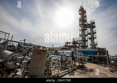 Grey oil distillation column on bright sun at a blue sky with clouds on oil refinery plant in a desert. Stock Photo