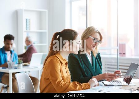 Two business partners sitting at the table and working on laptop together in team at office Stock Photo