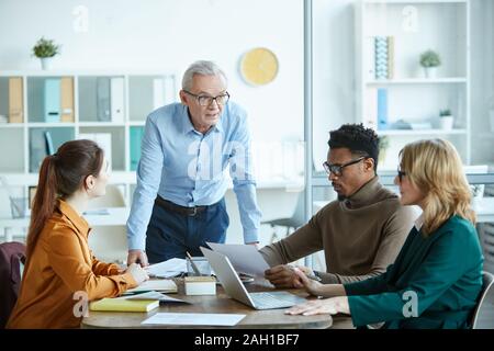 Multiethnic business people sitting at the table and listening to mature businessman during business meeting at board room Stock Photo