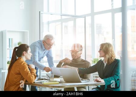 Group of business people discussing document and using laptop during team work at business meeting Stock Photo