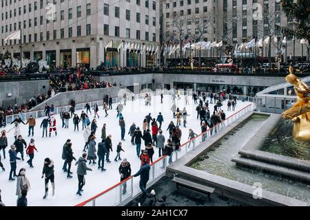 New York City - USA - DEC 17 2018: Seasonal ice skating rink with a golden statue, in a famed complex with upscale shops & restaurants in Rockefeller