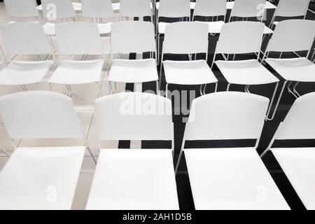 Rows of white plastic chairs for formal meetings, conference, lectures, graduation ceremonies. Room full of empty white chairs. Stock Photo
