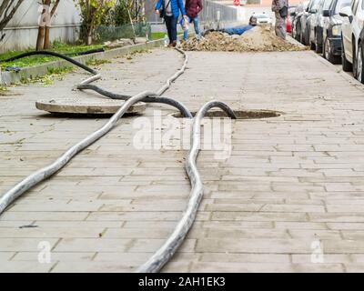 Laying of new cables in a manhole on the sidewalk. Opened hatch on the pavement while cables replacement. Underground construction and repair. Stock Photo