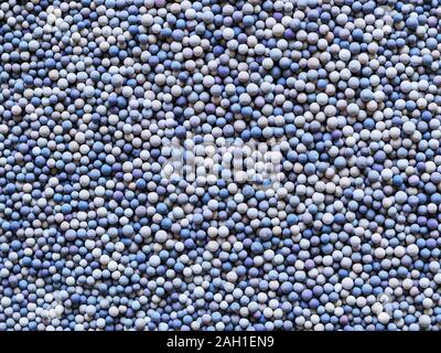 A lot of tiny ceramic balls or granules in color range from beige to dark blue as a background. Grainy or granular texture. Top view. Stock Photo