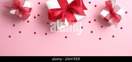 Valentine's Day banner with white gift boxes decorated red ribbon bow on pink background with confetti. Flat lay, top view. Stock Photo