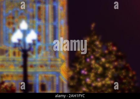 Colorful bokeh defocused christmas fairy lights, new year fair. Lantern on a background of yellow lights of illumination next to a Christmas tree. Stock Photo