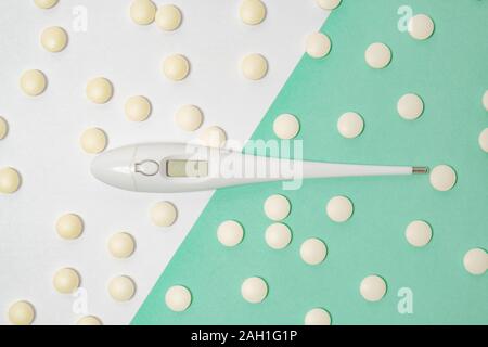 Electronic medical thermometer among yellow pills in two color background. Health issues, being cold, doing home treatment or having fever concept Stock Photo