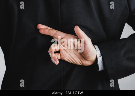 Having hopes for a good deal in business of being cuperstitious. Crossed fingers behind the back: concept of hoping for good luck or having risks Stock Photo