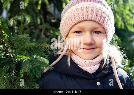 Little beautiful girl with lovely smile posing near fir tree in casual clothes Stock Photo