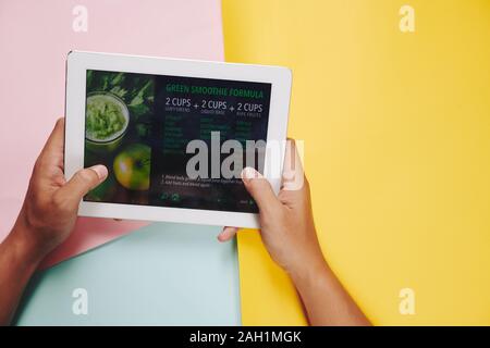 Hands of man holding tablet computer with green smoothie recipe on the screen Stock Photo