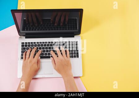 Hands of software developer working on laptop at his colorful desk, view from above Stock Photo