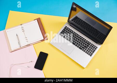 Opened laptop, planner and smartphone with earbuds on colorful desk of creative person, view from above Stock Photo