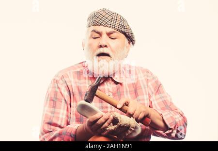 mature shoemaker in workshop make shoes. Cobbler workmanship. shoemaker working with leather textile and hammer at workshop. retro man repair shoes with hammer. shoemaker at work. at shoe store. Stock Photo
