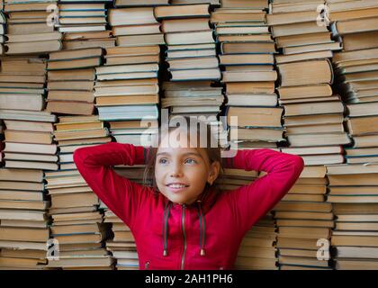 Close up portrait of a dreaming smiling schoolgirl over bookshelf background. Education and school knoweledge concept Stock Photo
