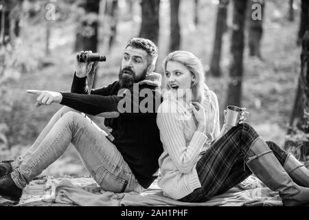 wild outdoor. couple in love relax in autumn forest with tea or coffee. camping and hiking. surprised girl drink mulled wine. bearded man shocked watch with binoculars. Spring mood. Family picnic. Stock Photo